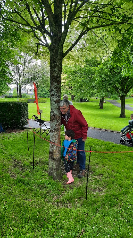 Listener with eyes closed, leaning against tree trunk, headphones visible. Contemplative, quiet.