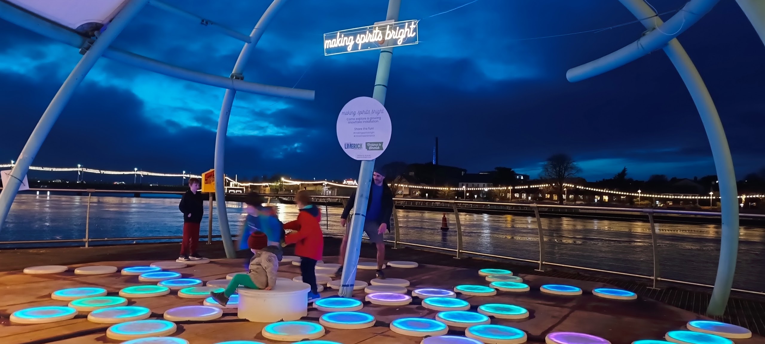 Making Spirits Bright, 72 LED snowflake pads on Harvey's Quay. Night-time, families stepping on glowing pads. Christmas 2025.