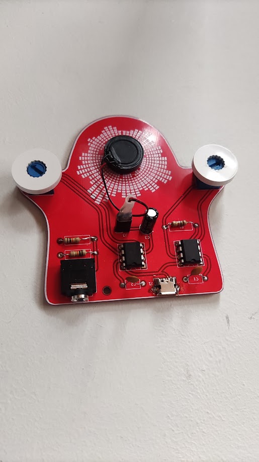 Voice coil pressed against a glass surface, wires trailing back to completed PCB. The moment of first sound.