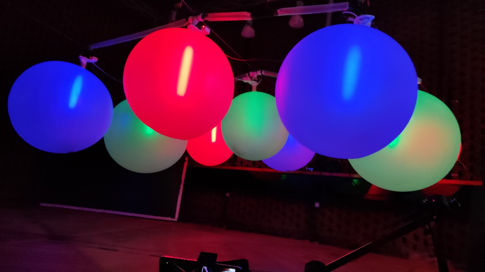 Full installation view, multiple balloons inflated at different sizes, shimmering with colour in the space.
